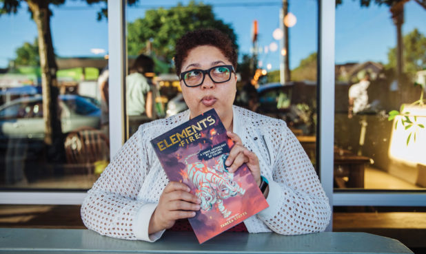 Taneka Stotts sits at a table holding a comic anthology.