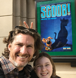 Man and his daughter in front of movie poster with dog on it
