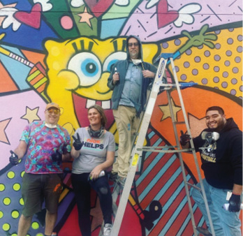 Group of people in front of colorful SpongeBob mural.