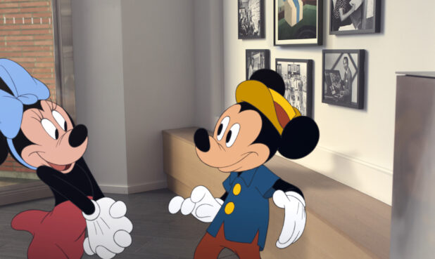 Minnie Mouse speaking to Mickey Mouse at the Disney Studios, in front of pictures of Walt Disney.
